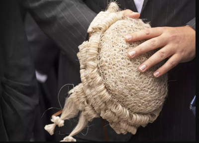 Body shot of a judge's black gown. Man holding wig